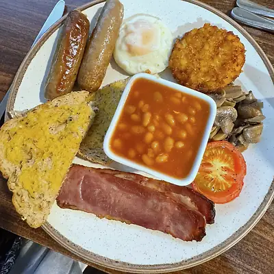 Breakfast plate with sausages, fried egg, hash brown, mushrooms, grilled tomato, a rasher, beans and toast