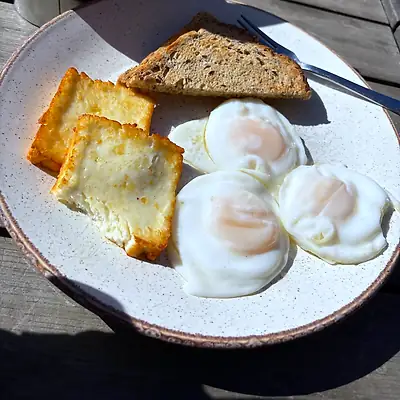 Plate of fried eggs, grilled halloumi and seeded toast on a wooden outdoor table
